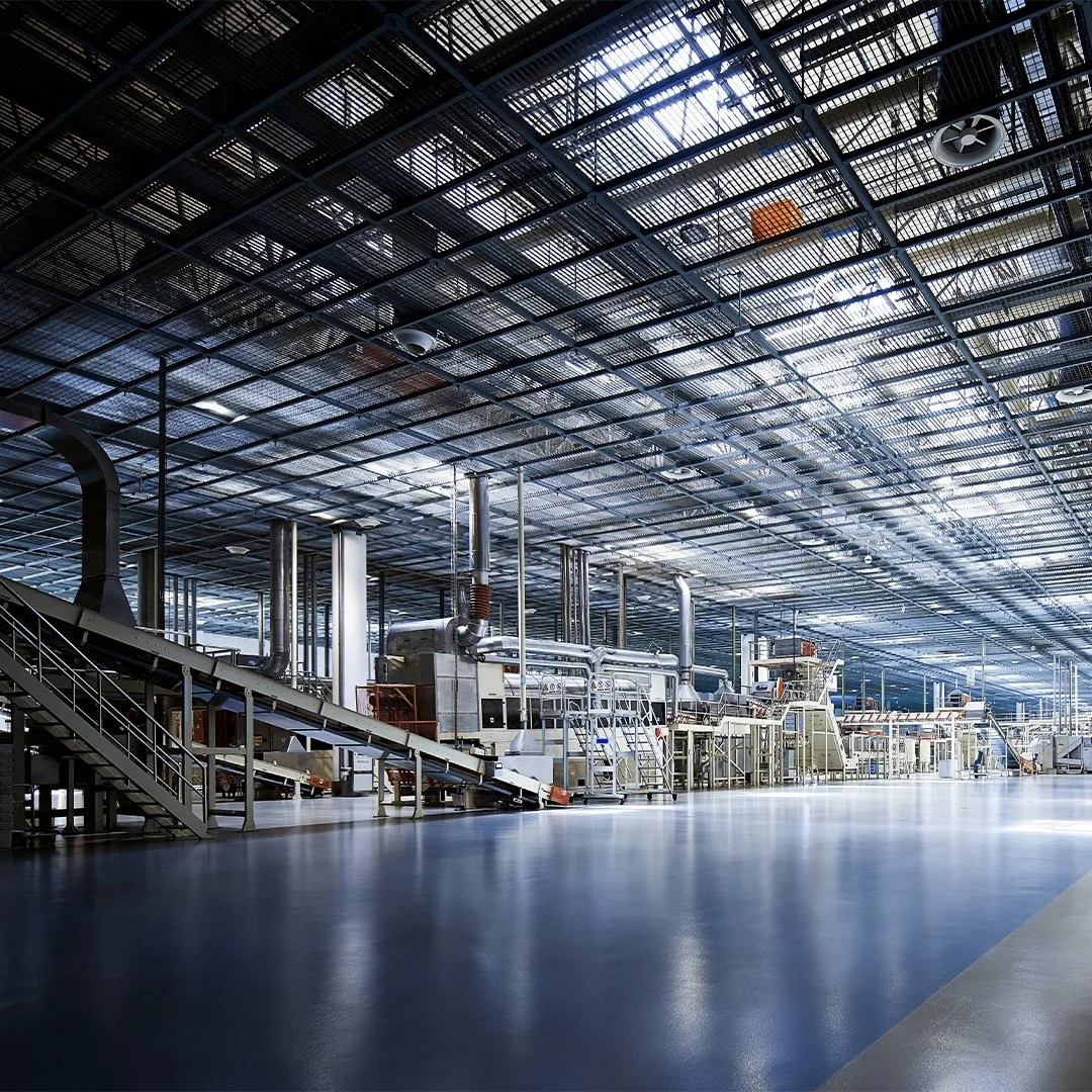 An empty industrial factory or warehouse with large machinery and metallic structures, and a shiny floor reflecting light from above. مصنع الفولاذ في مدينة جدة