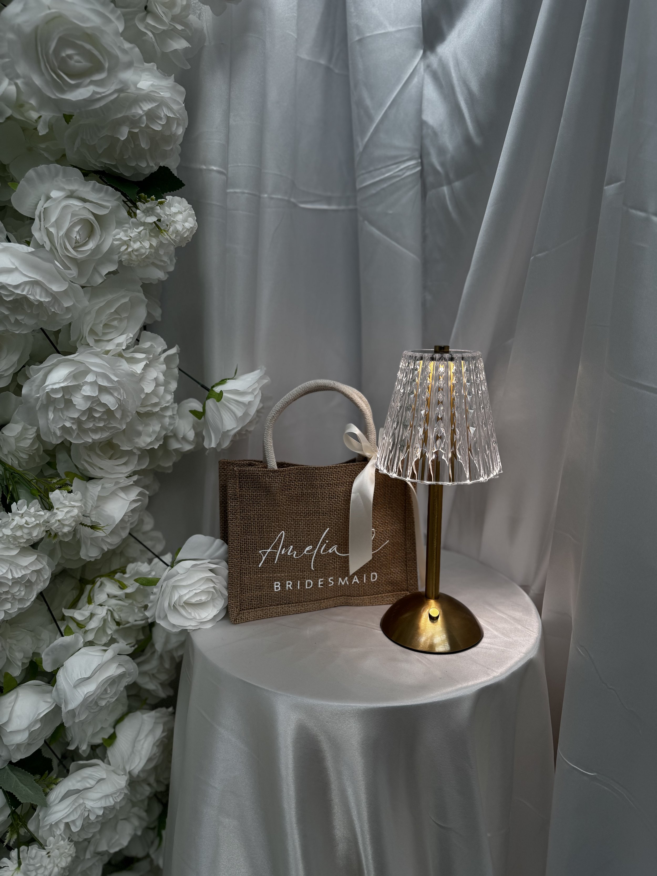 Luxury custom bridesmaid proposal bag sitting on a table with a glowing lamp. Personalised natural jute bridesmaid gift bag with elegant ribbon tie by Storymade