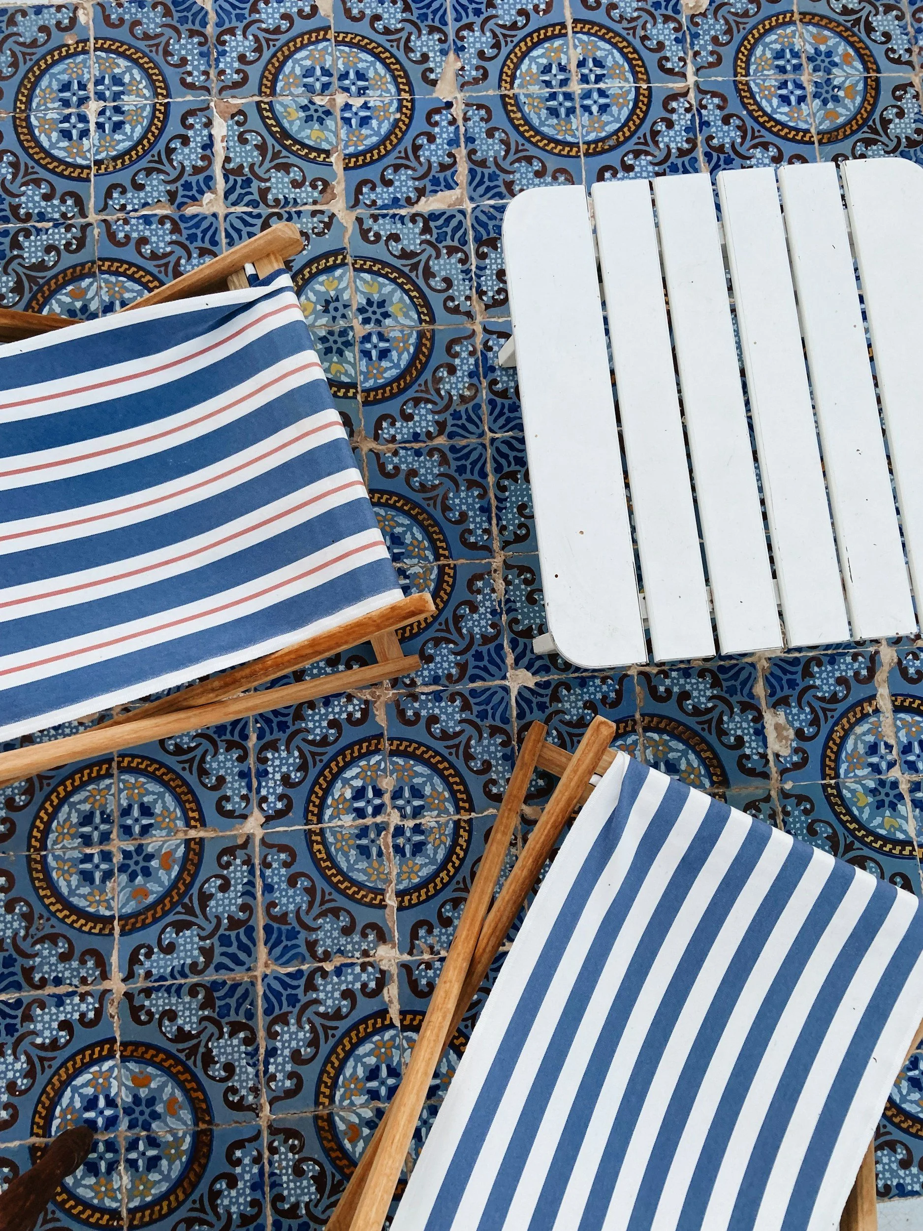 Two striped deck chairs with wooden frames on patterned blue and gold decorative tile floor, along with a white wooden table.