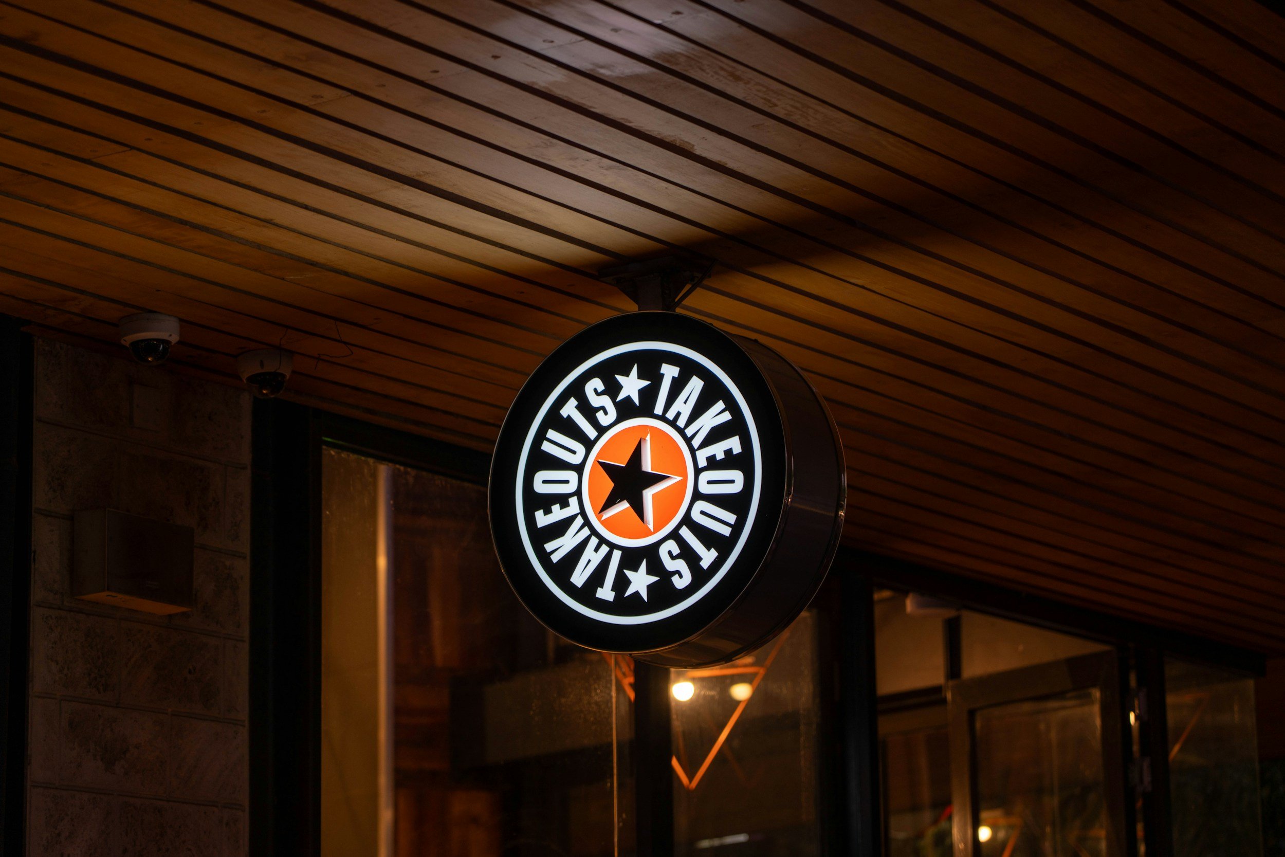 Illuminated circular sign for Taco Bell with the text "Taco Bell Mexican Cuisine" and a star in the center, hanging outside a restaurant.