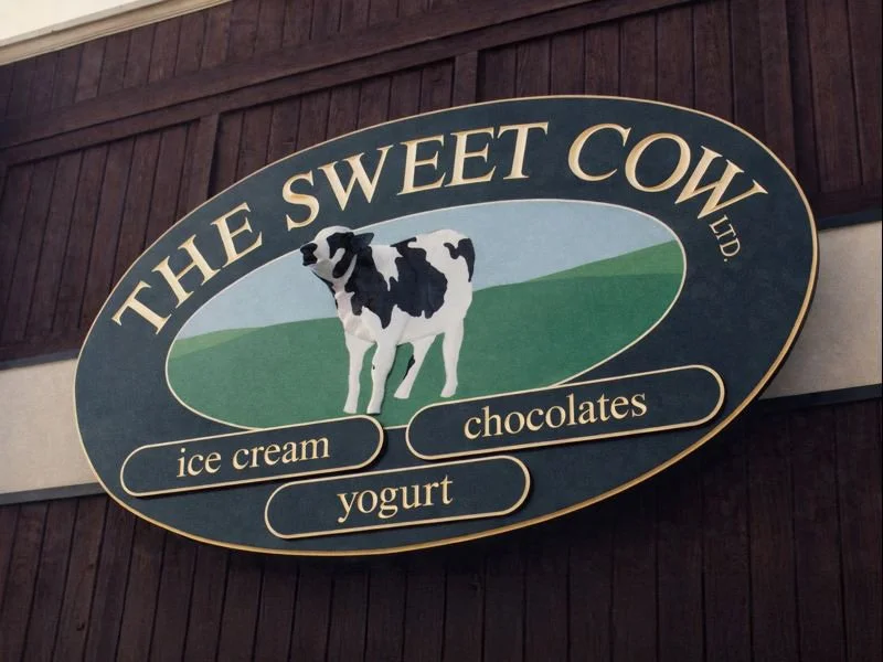 Sign for The Sweet Cow, featuring a black and white cow illustration and listing ice cream, chocolates, and yogurt.
