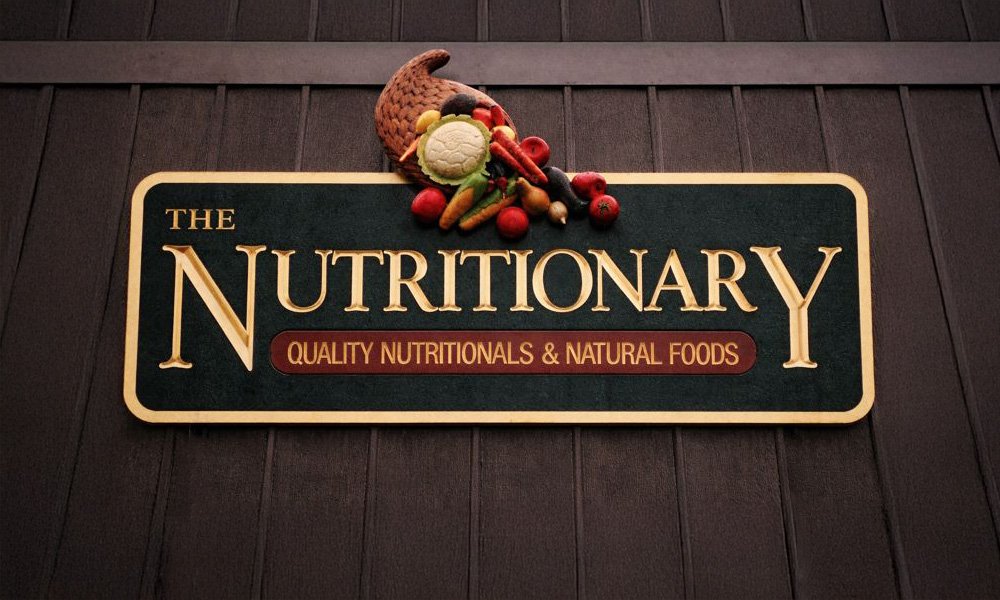 A sign for The Nutritionary, a store specializing in quality nutritionals and natural foods, mounted on a wooden wall.