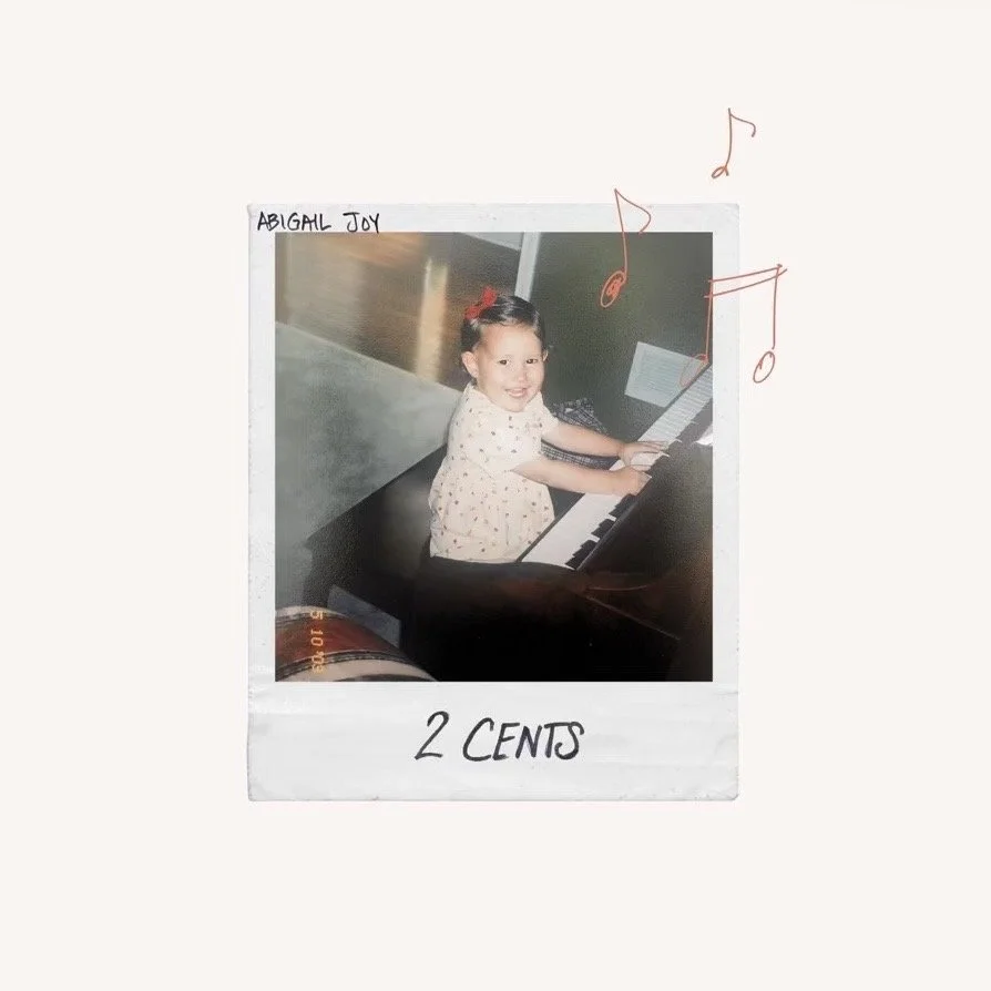 A young girl smiling and playing a piano, with a handwritten label 'Abigail Joy' at the top and '2 cents' at the bottom, along with musical notes drawn on the photo.