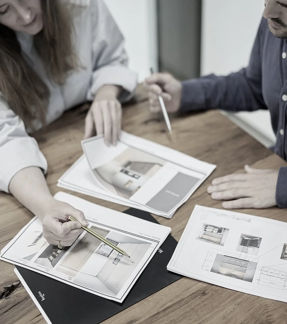 Deux personnes discutant autour de plans et de brochures architecturales sur une table en bois.