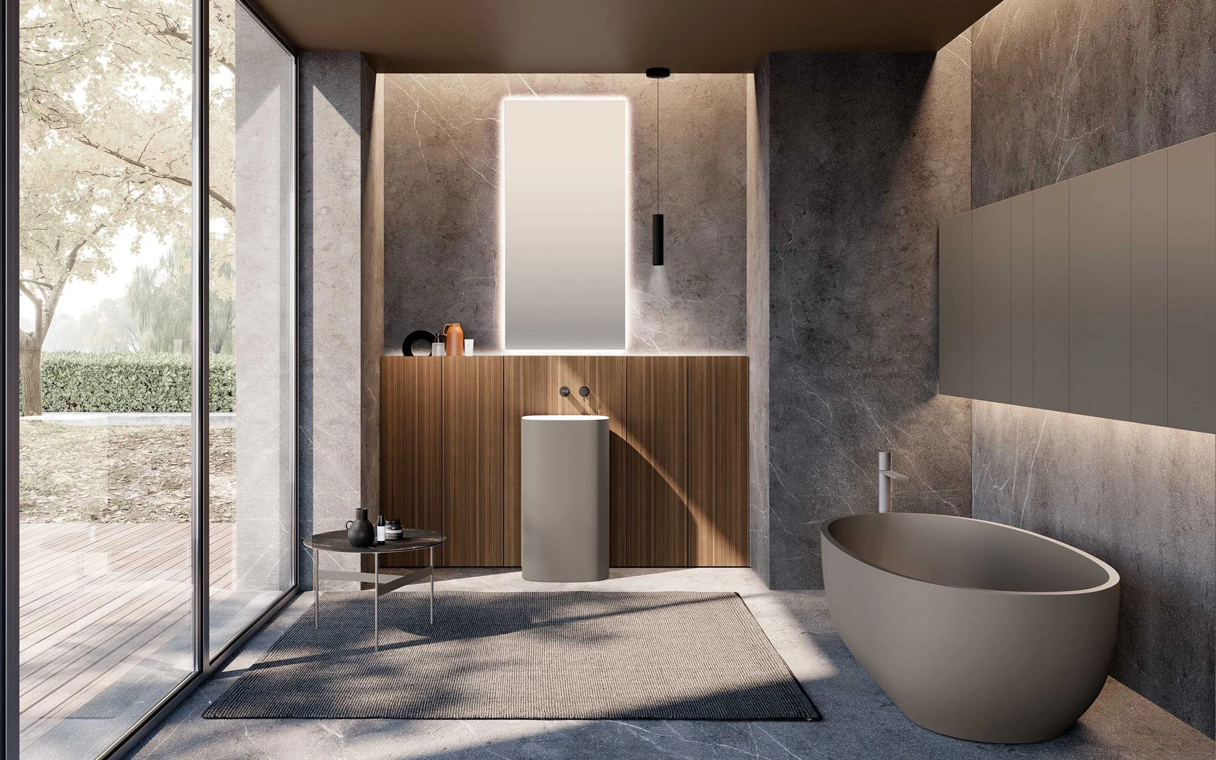 Une salle de bains moderne M3 system, une baignoire ovale beige, un meuble en bois et en laque, un miroir  lumineux, et des décorations minimalistes. Sol en pierre, murs en pierre grise, tapis gris, et vue extérieure avec arbres et nature.