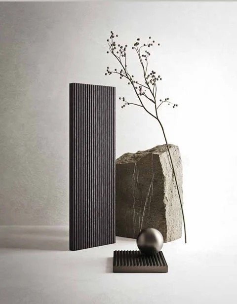 Composition minimaliste avec un rocher, une branche avec des baies, une sphère métallique, une planche noire, et un panneau vertical rayé, tous disposés sur un fond neutre.