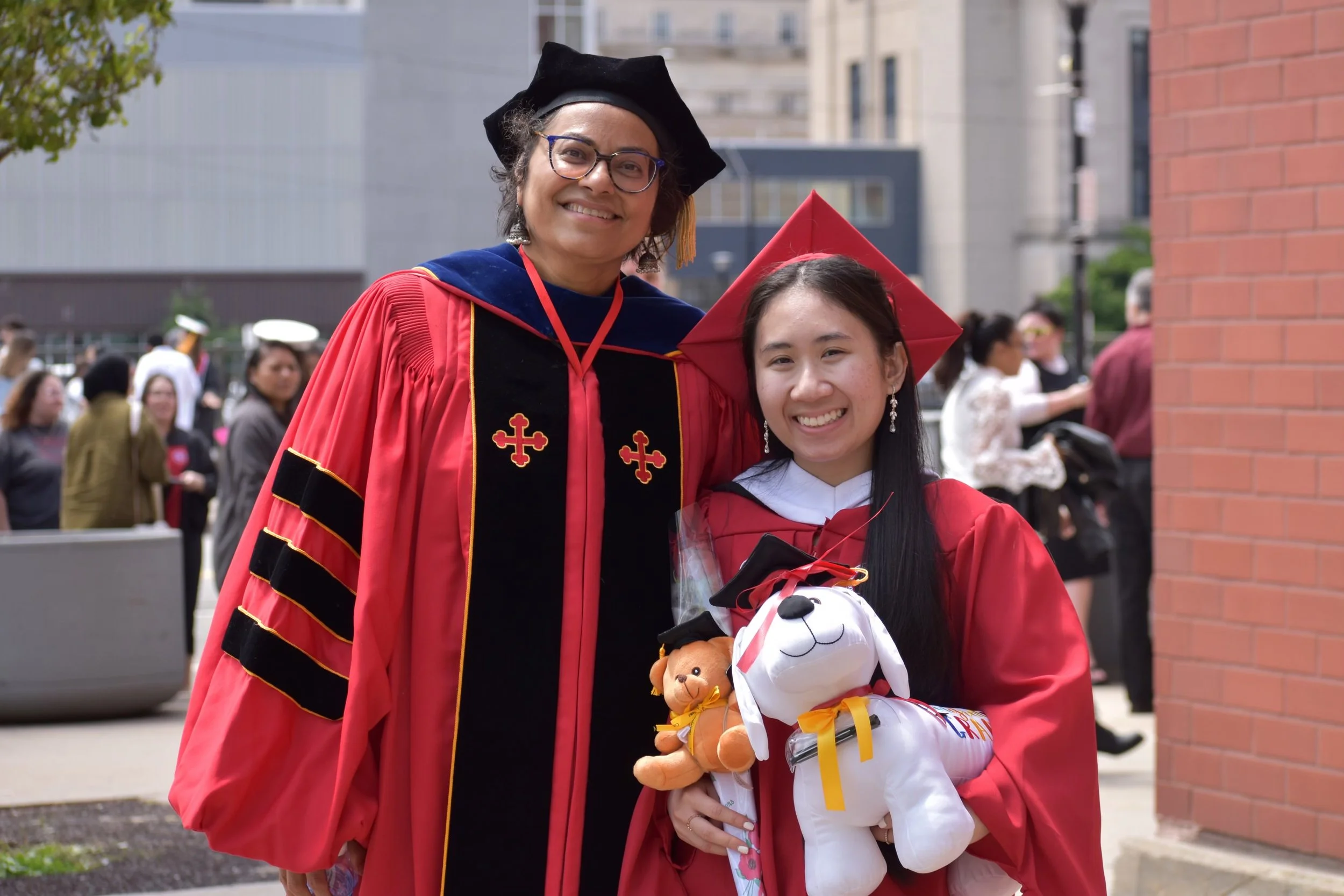 Naomi and her professor in academic regalia, smiling at graduation ceremony outdoors.