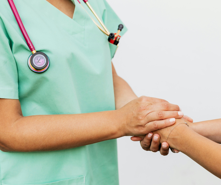A healthcare professional in green scrubs holding a patient's hand.