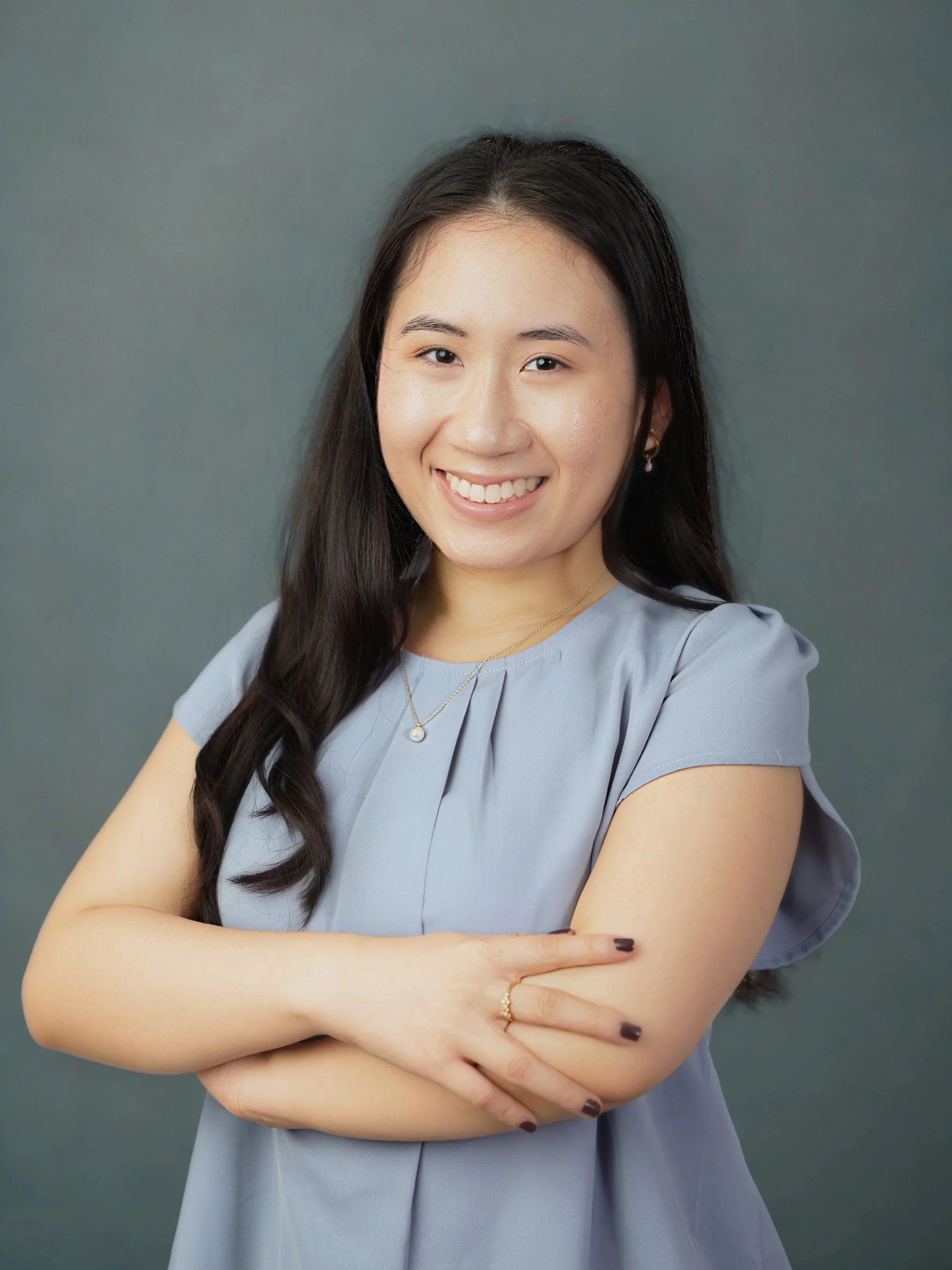 Naomi smiling with arms crossed in front of gray background.