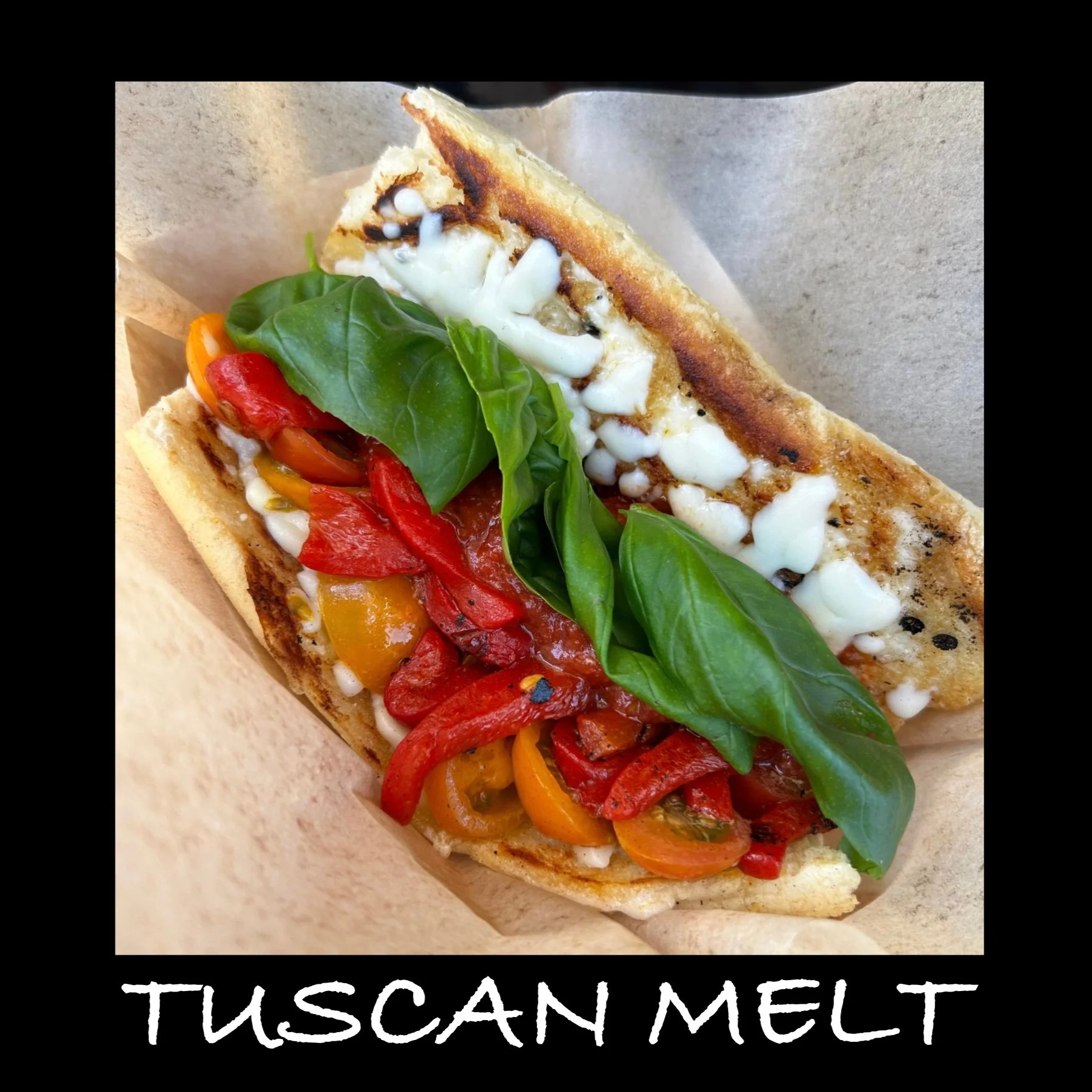 A sandwich with grilled bread, fresh basil leaves, colorful roasted red and yellow bell peppers, and melted cheese, labeled as 'Tuscan Melt'.