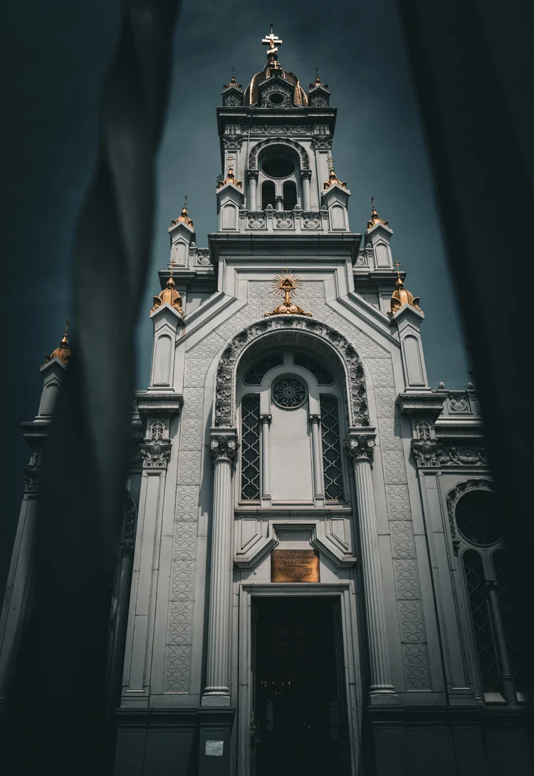 An ornate church facade and bell tower framed by dark foreground edges against a blue-gray sky.