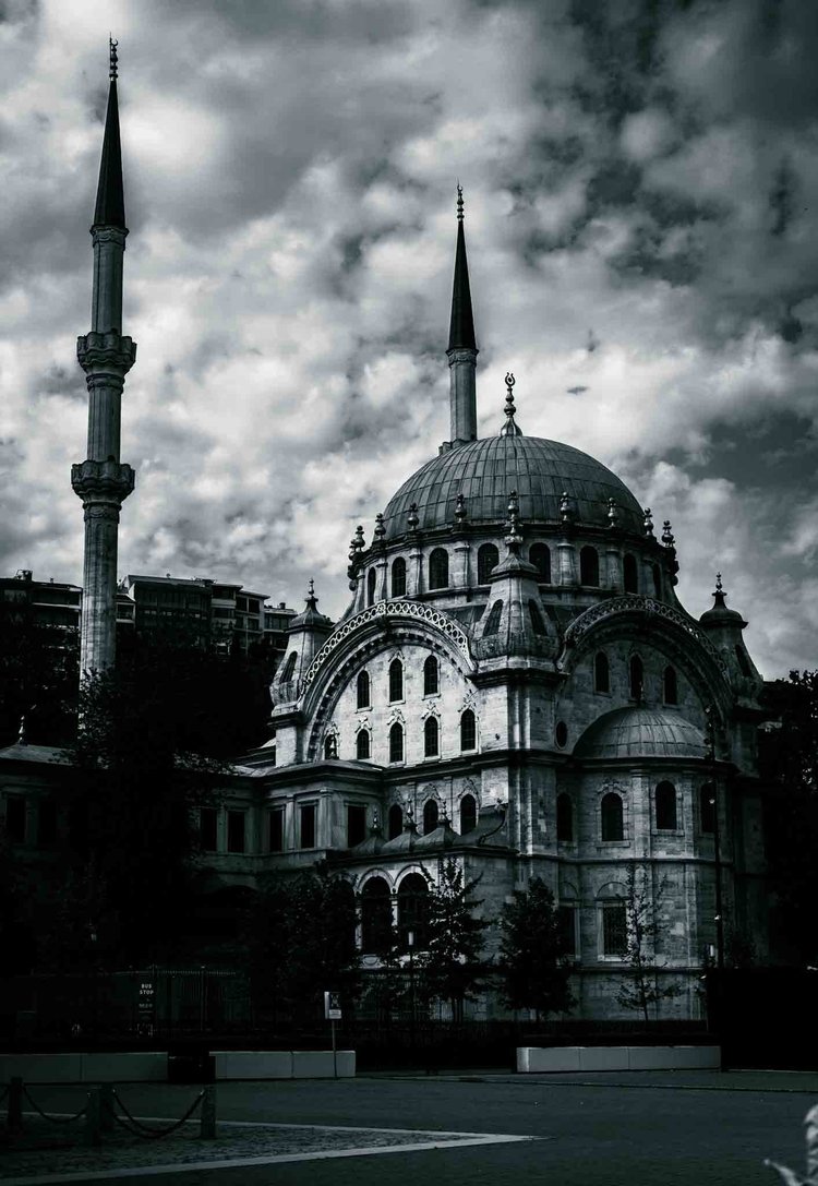 A domed mosque with two slender minarets beneath a cloudy sky, seen from the street.