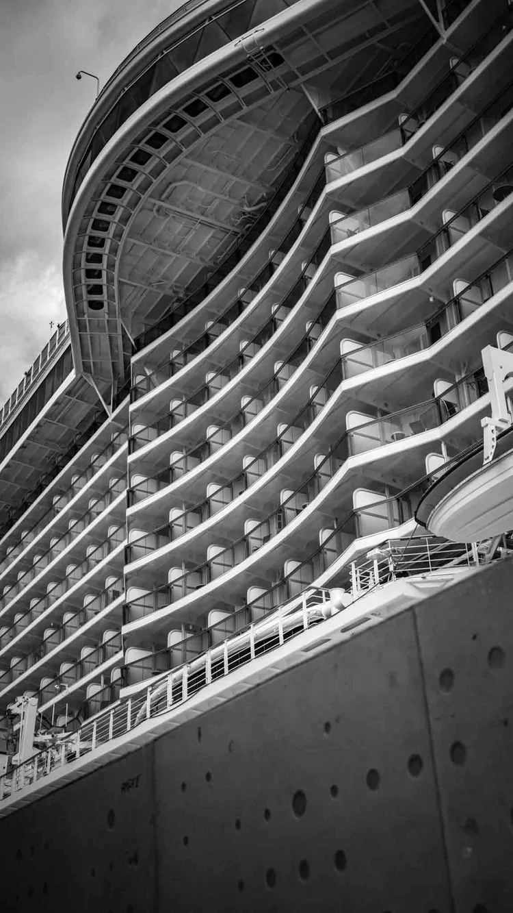 Black-and-white upward view of a passenger ship’s curved superstructure and repeating balcony decks.