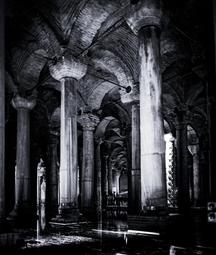 Rows of illuminated stone columns recede into a dark vaulted cistern, photographed in black and white.