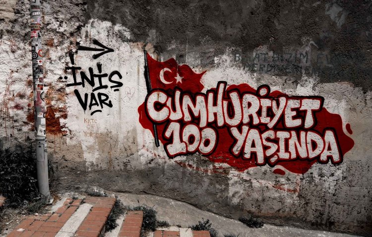 Red-and-white graffiti reading “Cumhuriyet 100 yaşında” beside a Turkish flag motif on a weathered wall.