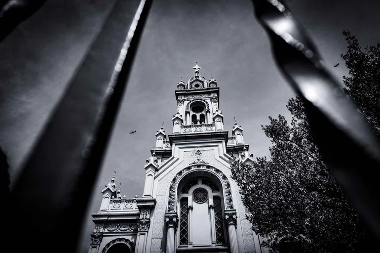 An ornate church facade and bell tower framed between dark metal railings, in black and white.