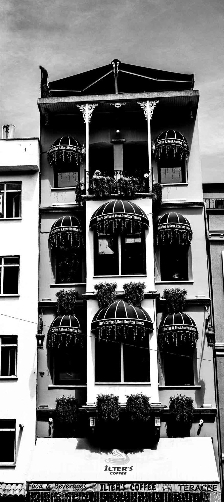 Black-and-white portrait-format view of a narrow ornate building with arched windows and a top-floor balcony.