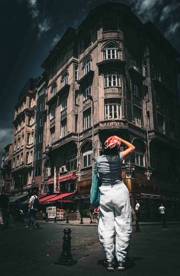 A person in a red cap stands at a street corner beneath an ornate multi-story building.