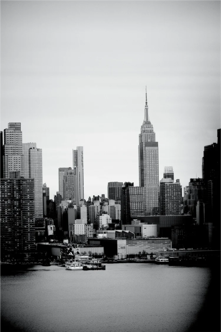 Black-and-white view of the Empire State Building and surrounding Manhattan skyline across the water.