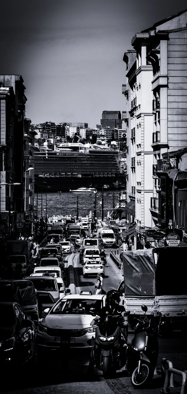 Black-and-white view down a busy city street filled with cars and framed by closely spaced buildings.
