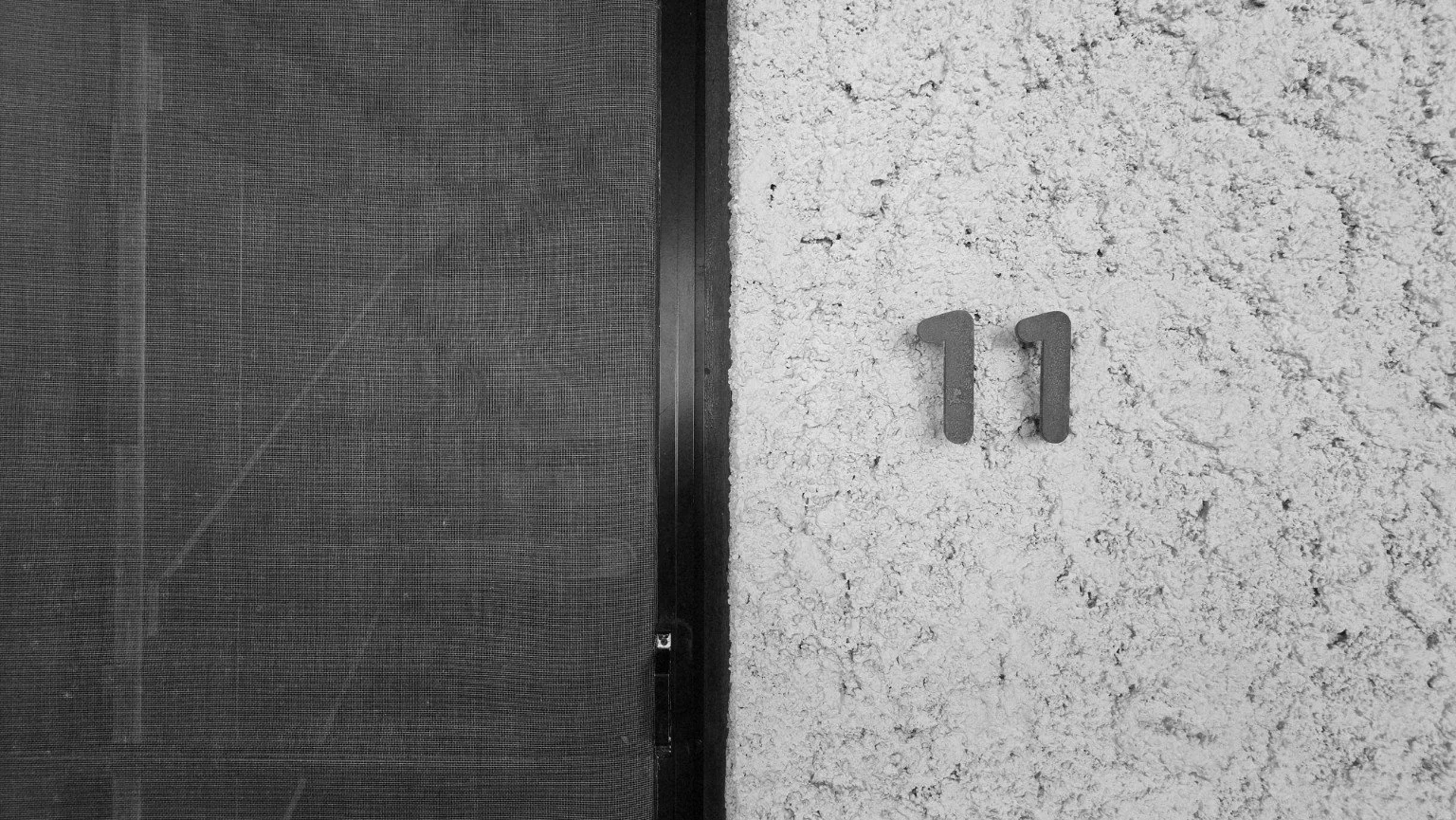 Black-and-white close-up of the number 11 on a textured wall beside a dark mesh door.