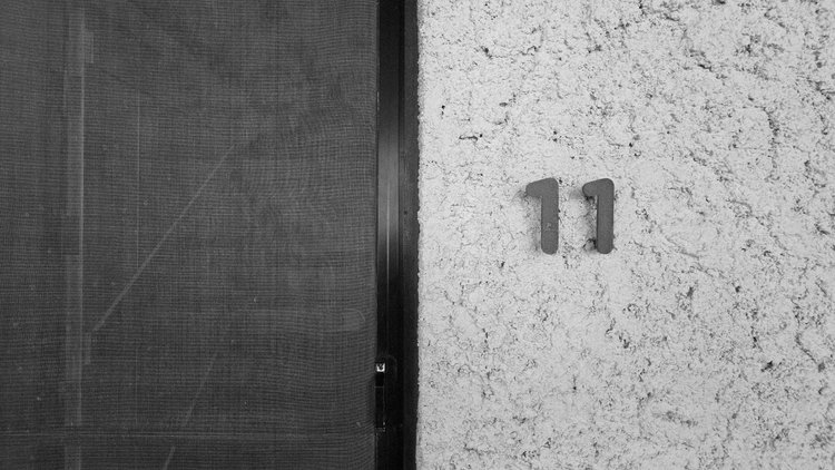 Black-and-white close-up of the number 11 on a textured wall beside a dark mesh door.