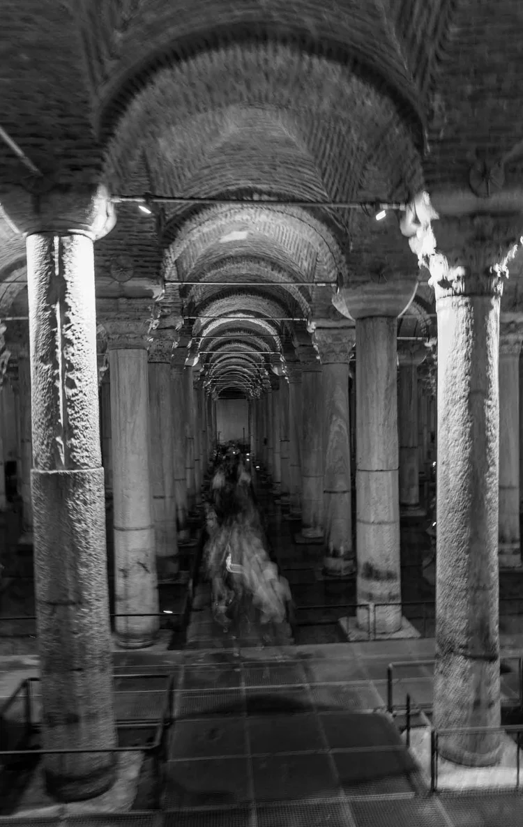 A long view through repeating stone arches and columns toward a central sculptural form.