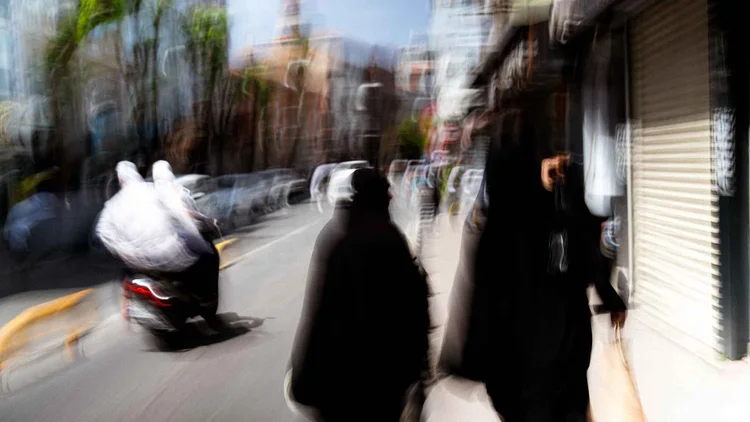 A motion-blurred street scene with pedestrians in dark clothing and a passing scooter.