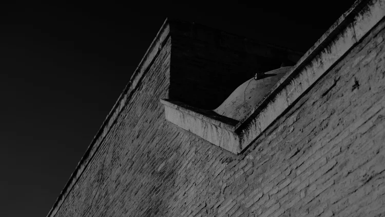 Black-and-white architectural detail of angular stone walls meeting against a dark sky.