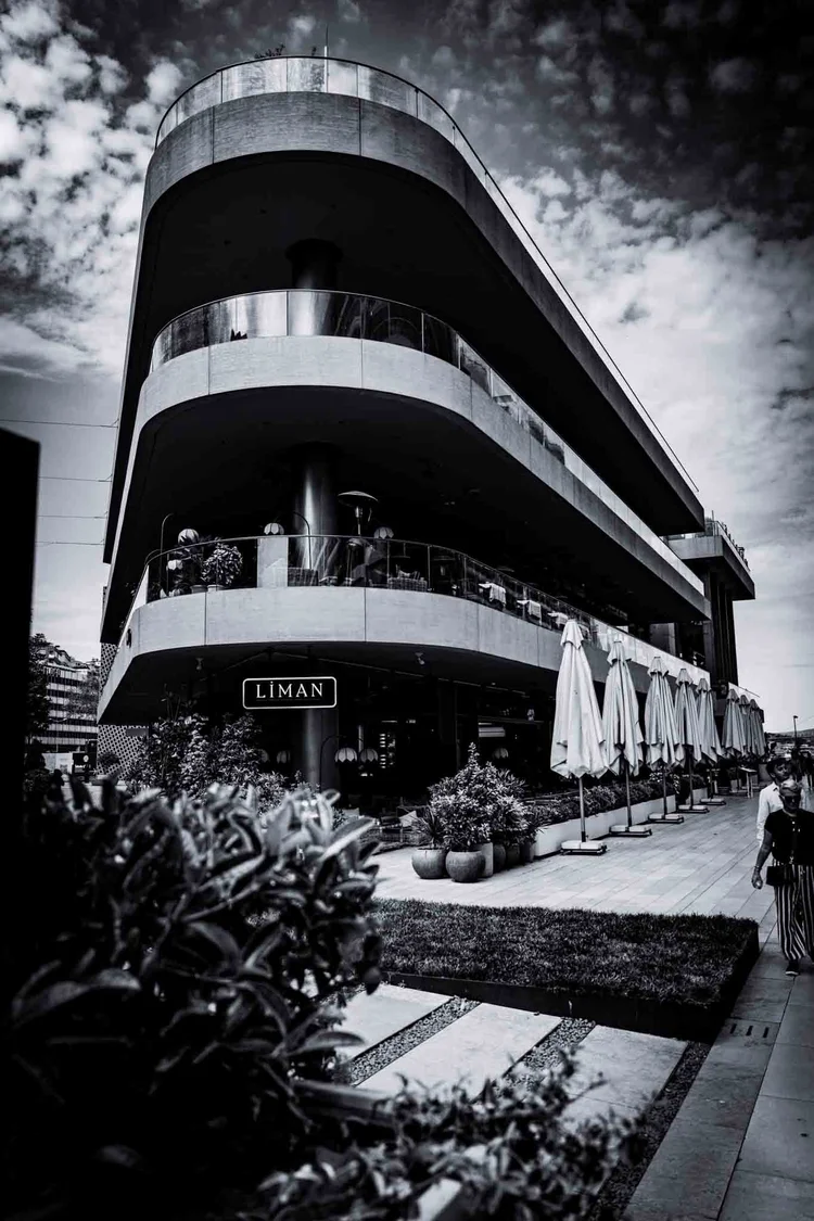 Black-and-white view of a modern corner building with sweeping curved balconies beside an outdoor seating area.