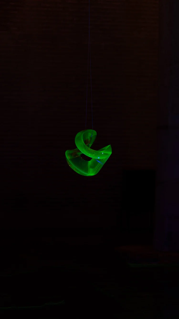 A small green illuminated sculpture surrounded by deep shadow in a brick interior.