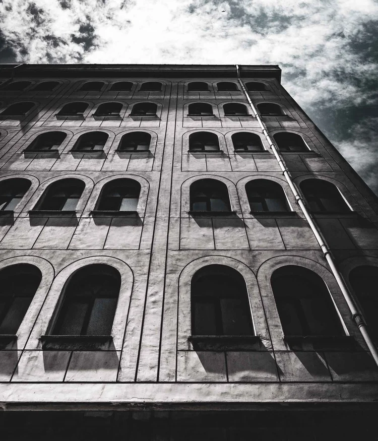 Black-and-white upward view of a stone building with rows of arched windows.
