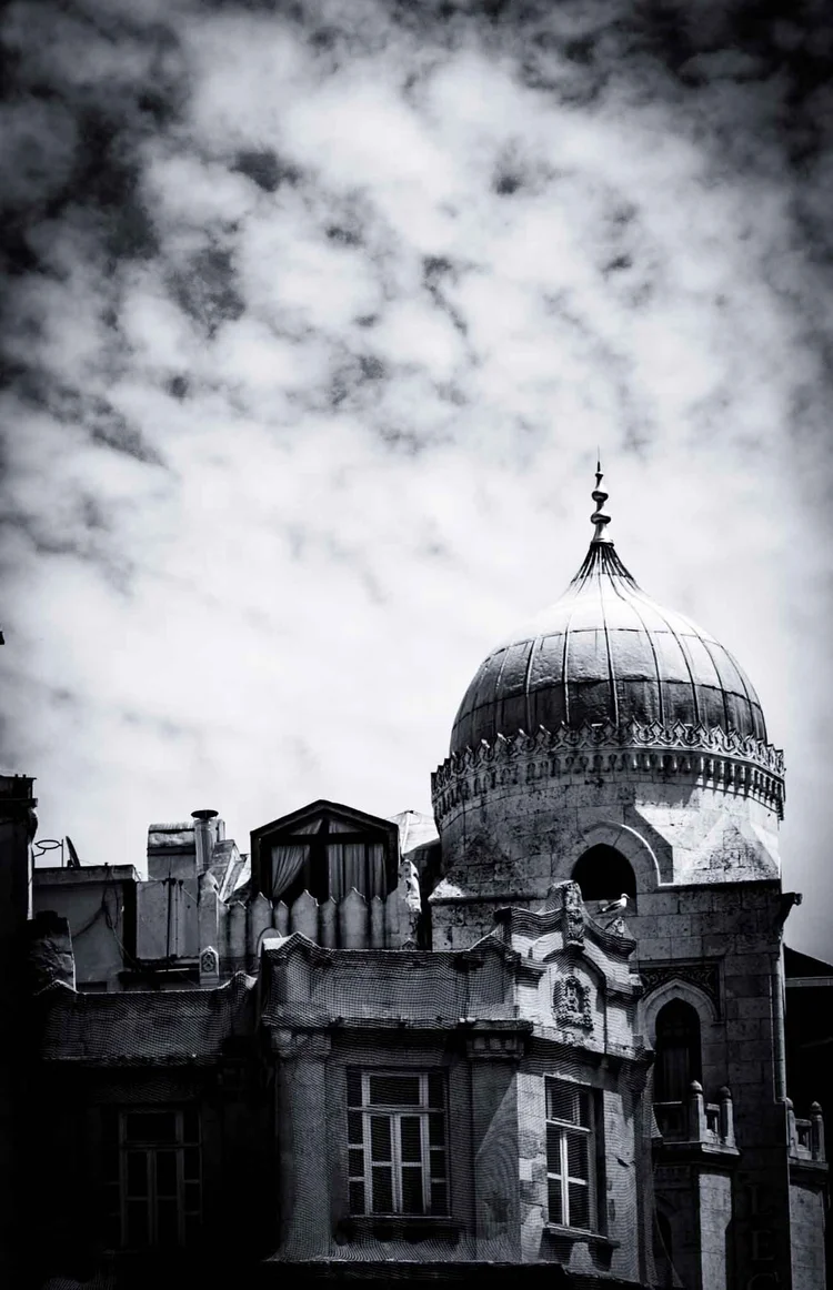 Black-and-white photograph of a weathered ornate building with a domed turret beneath textured clouds.