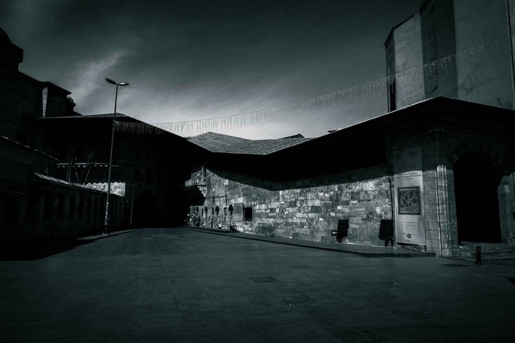 A broad, empty courtyard enclosed by stone buildings and an angular roof beneath a dark sky.