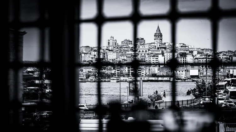 Black-and-white view of waterfront buildings and a distant tower through a square-paned window.