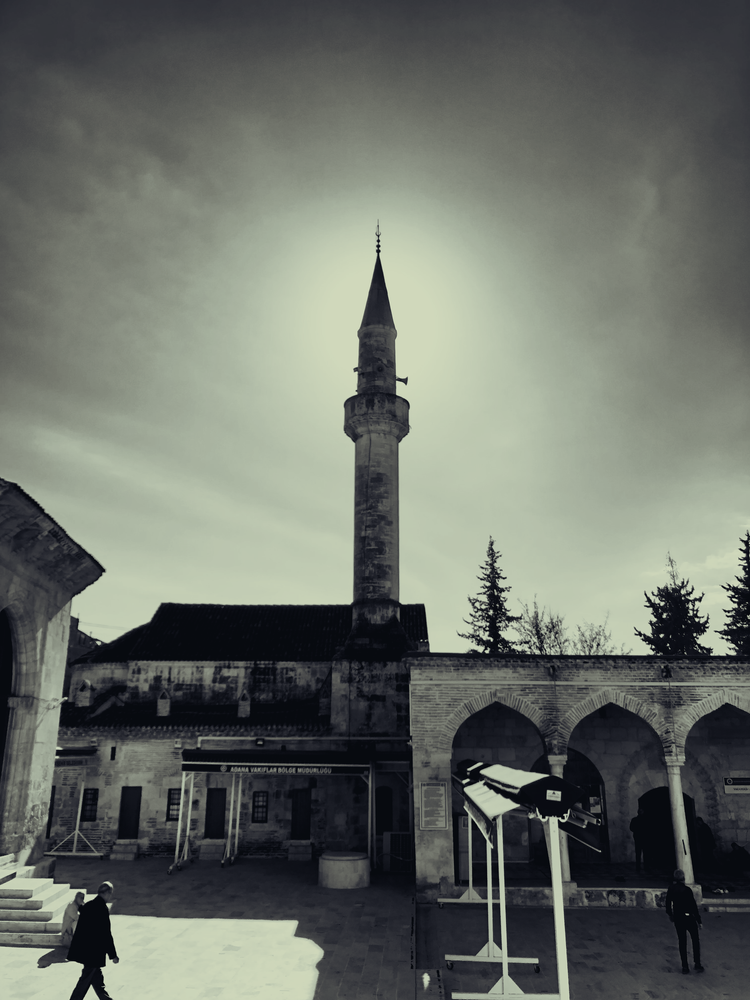 A mosque courtyard and tall minaret silhouetted against a softly glowing, clouded sky.