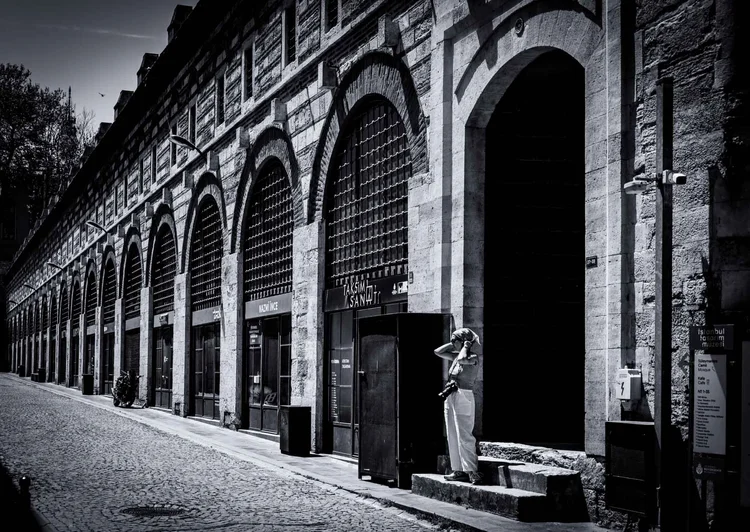 Black-and-white view along a cobbled street lined with tall stone arches, with a person standing in a doorway.