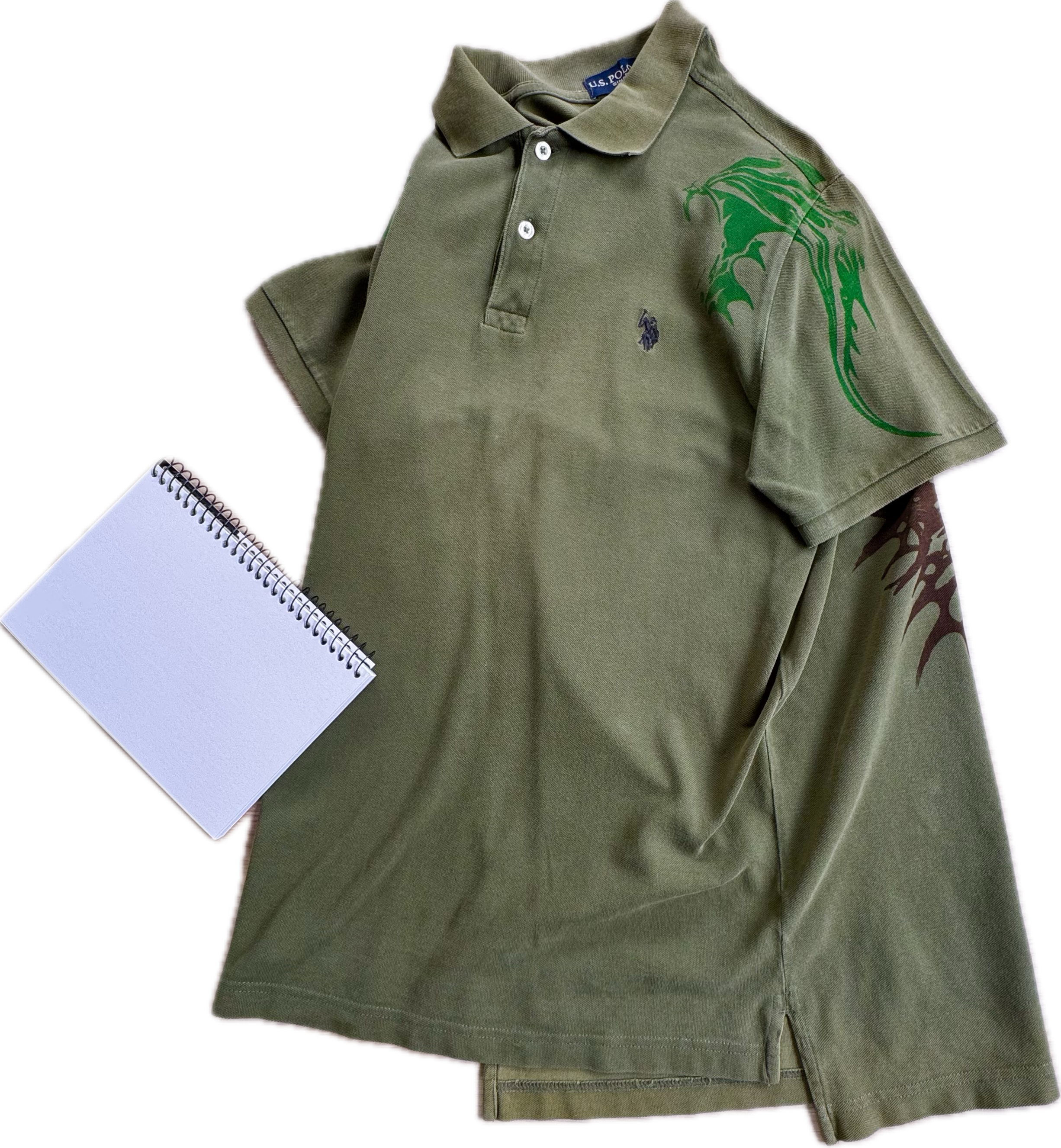 Green polo shirt with dragon and tribal designs and a notepad.