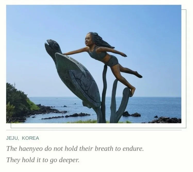 A sculpture of a woman flying over the ocean, with the ocean and a rocky shoreline in the background, located in Jeju, Korea.