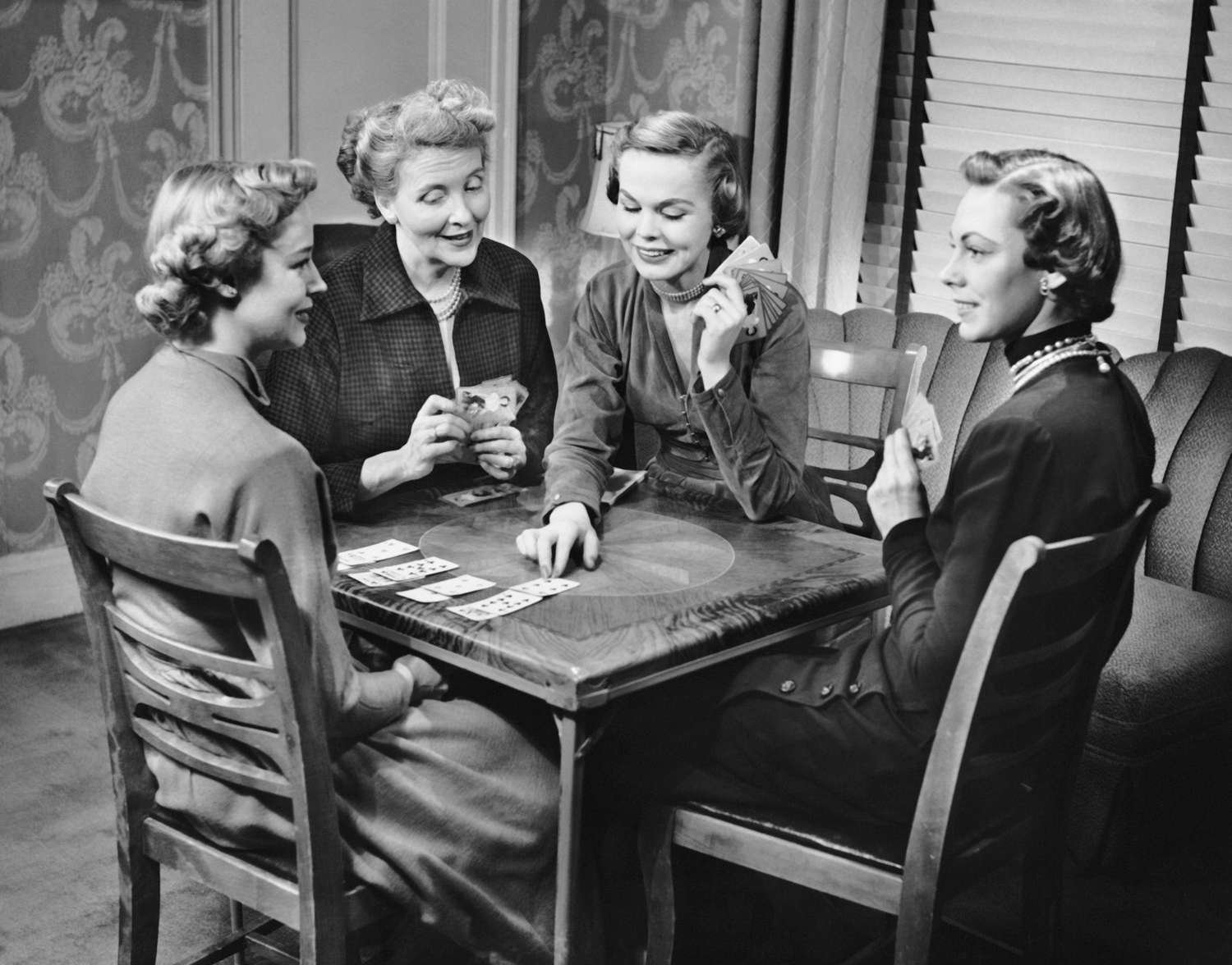 Five women sitting around a table playing cards in a living room.