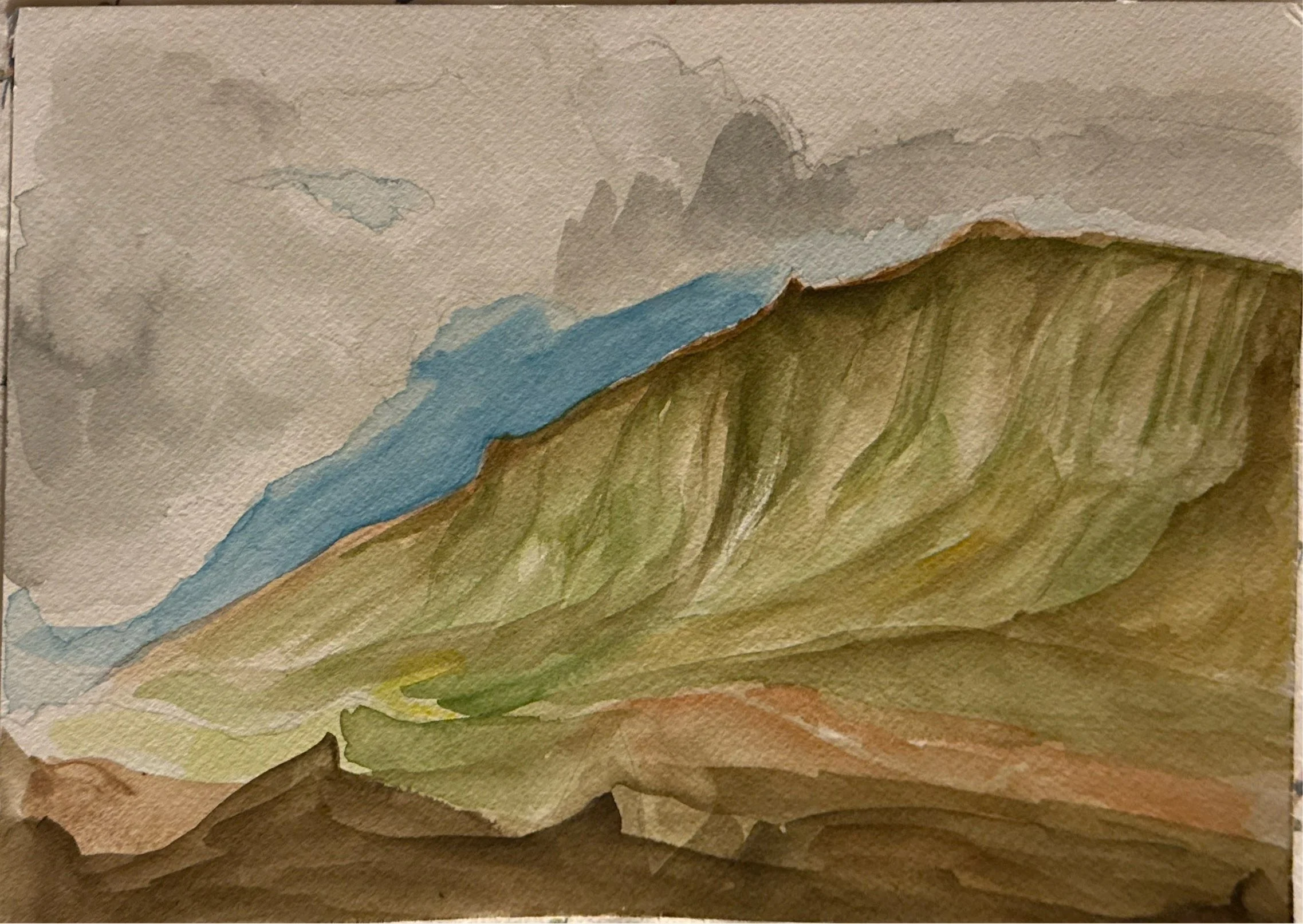 Watercolor painting of a mountain landscape with gray clouds, a blue mountain ridge, and green and brown hills in the foreground.