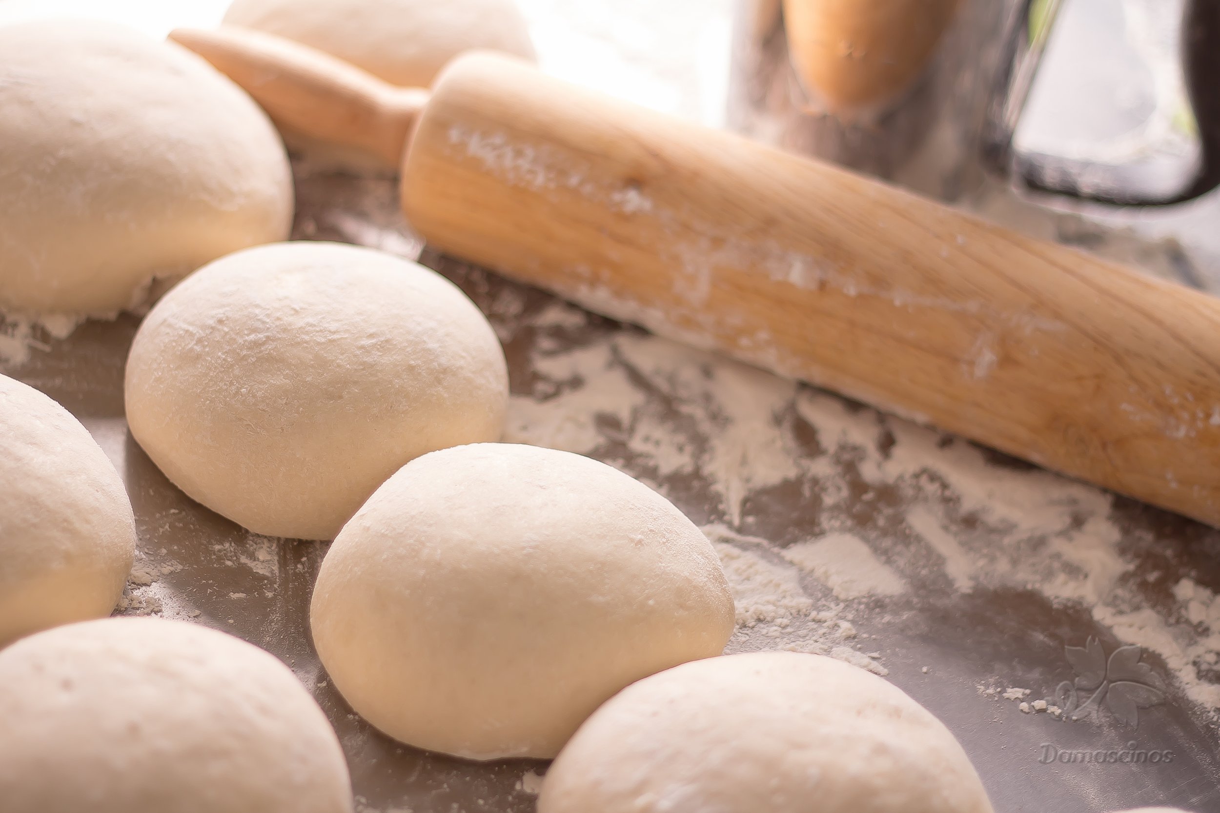 Dough balls on a floured surface with a rolling pin and a glass container nearby.