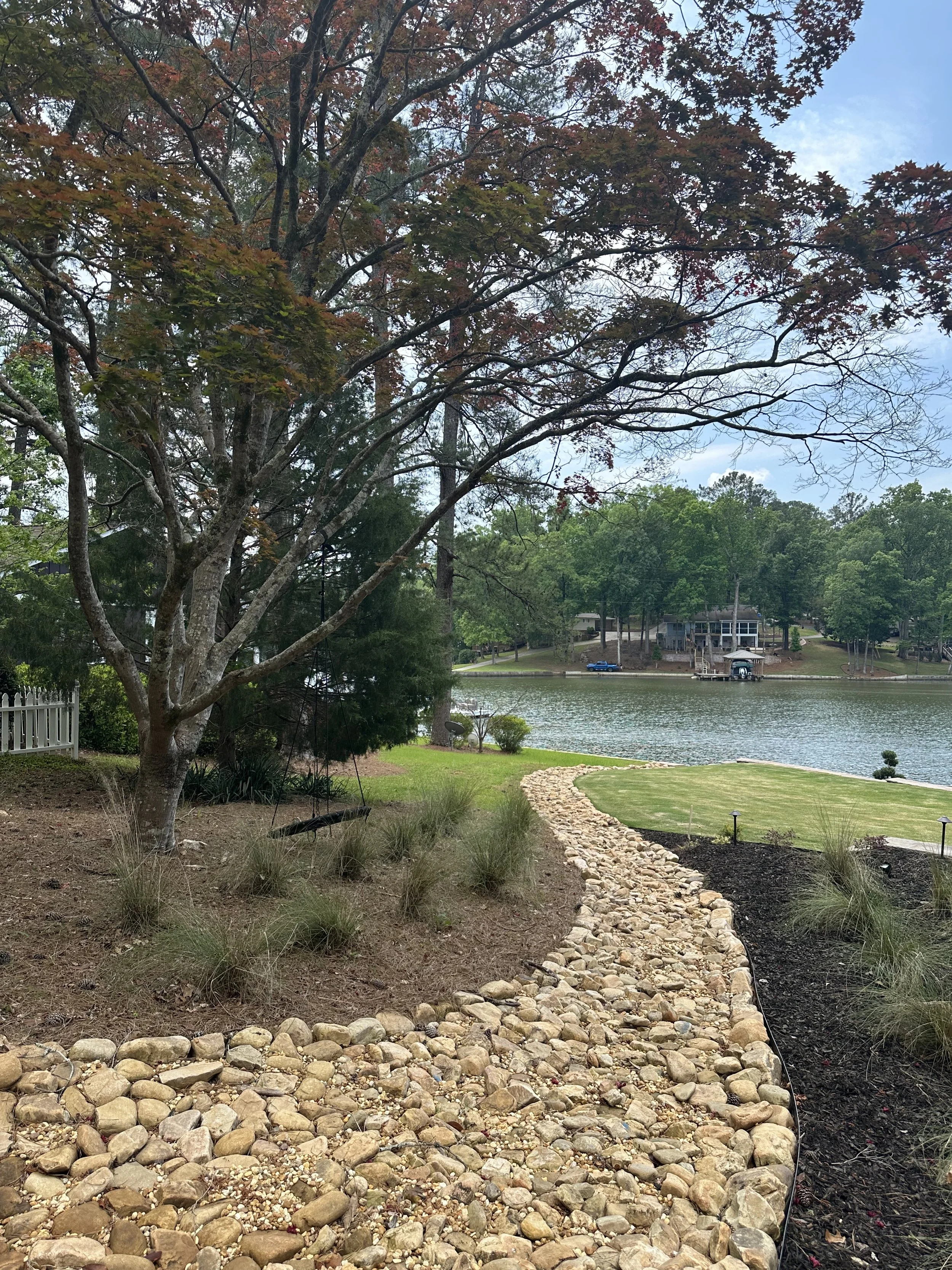 A landscaped yard next to a lake, featuring a stone pathway, grass, and trees.