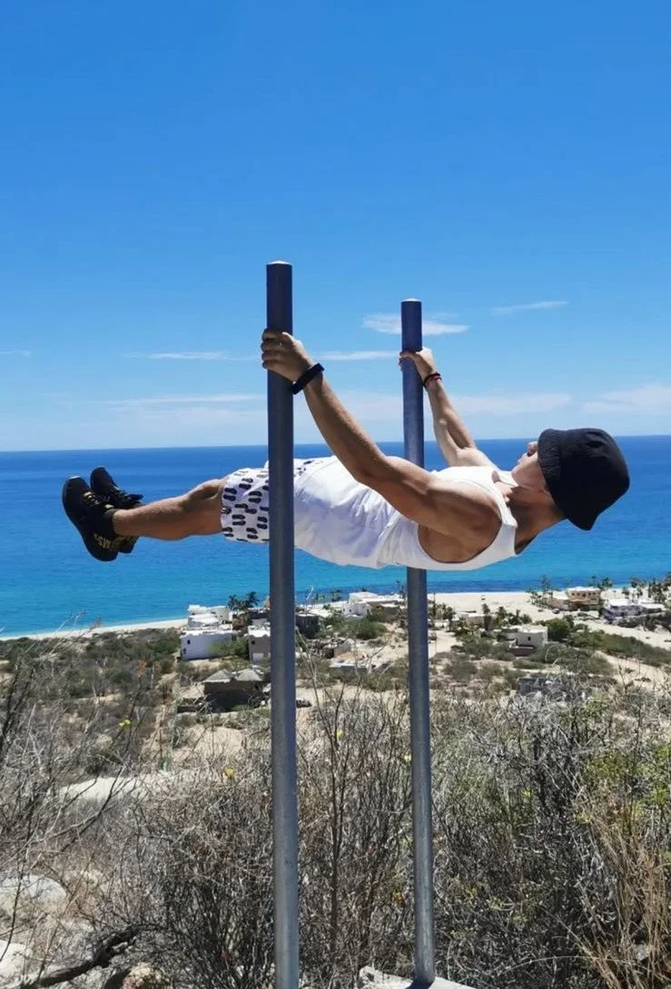 Persona haciendo ejercicio en barras paralelas al aire libre con vista al mar y paisaje costero en el fondo.