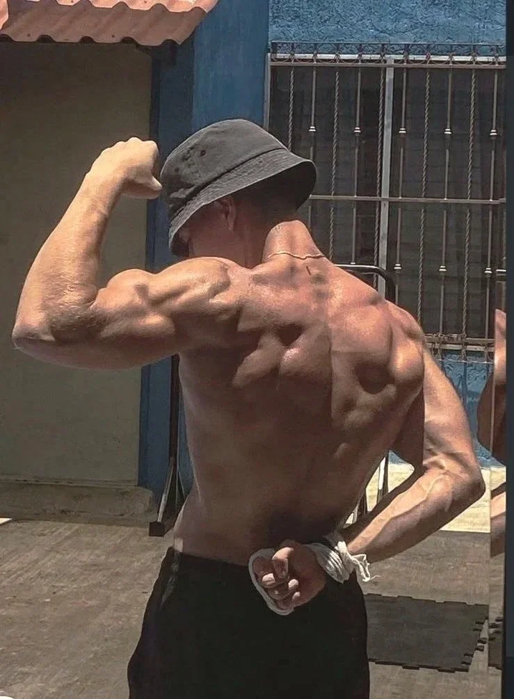 Hombre musculoso usando gorro de pescador , mostrando sus músculos del brazo y de la espalda en un espejo