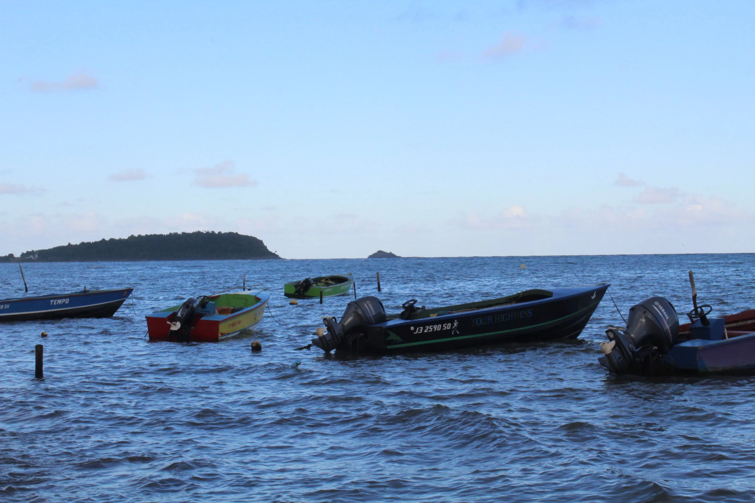 Several small boats with outboard motors floating on the water near a distant shore with islands and a partly cloudy sky.