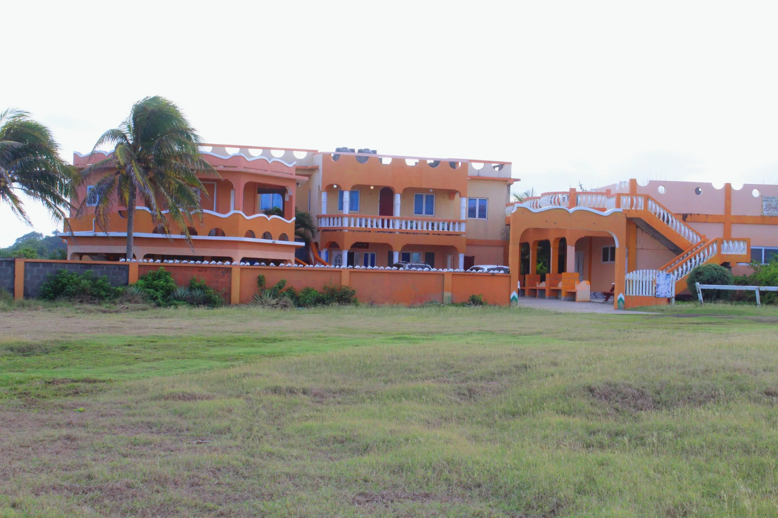 Multiple orange-colored buildings with white accents and staircases, surrounded by grass and palm trees.