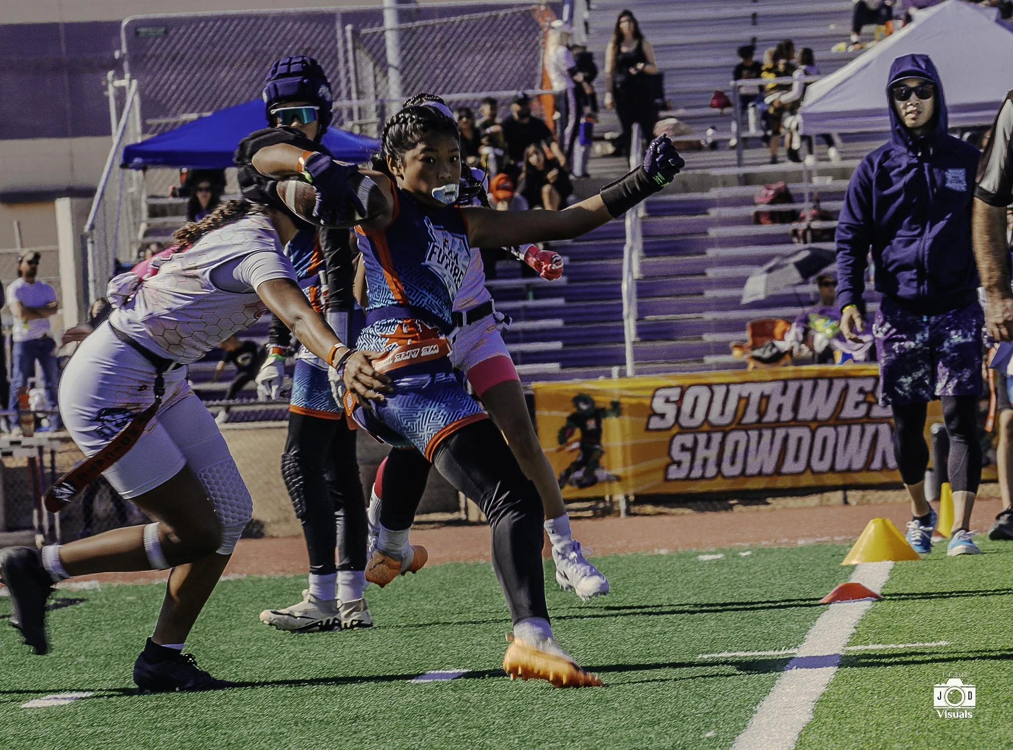 A group of athletes participating in a sprint race on a track at a sports event, with spectators in the bleachers and a banner that reads 'Southwest Showdown' in the background.