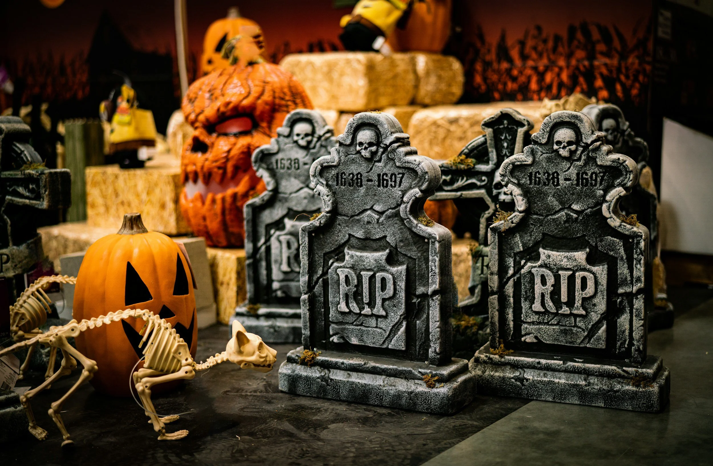 Halloween decorations including a plastic pumpkin with a carved face, a plastic skeleton, and several tombstone props with 'RIP' markings, set among other spooky items.