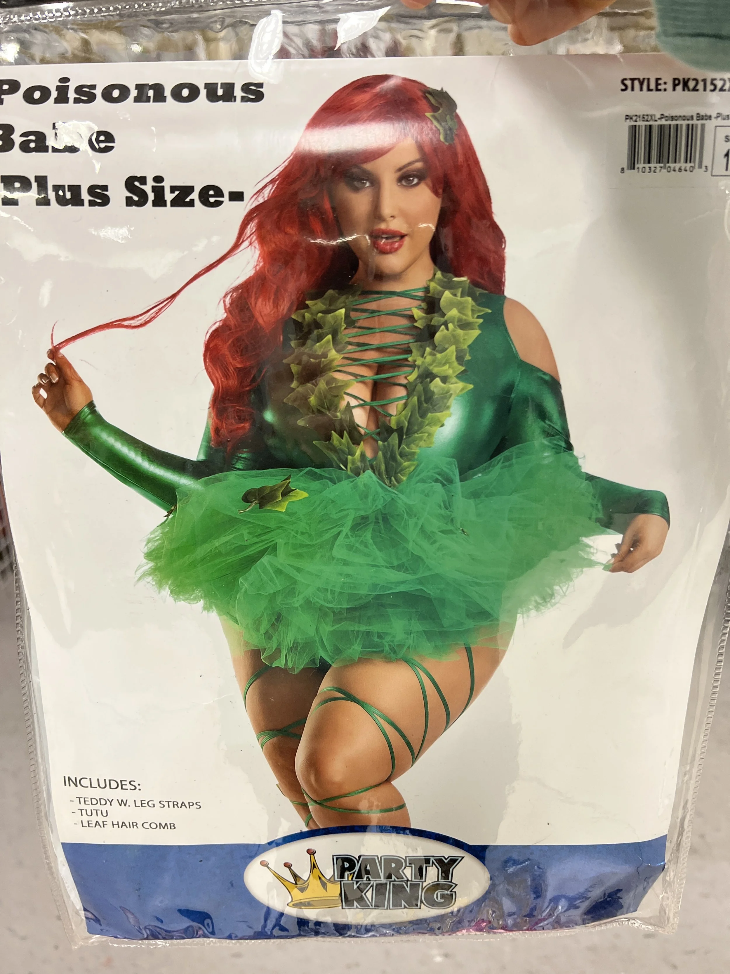 A woman dressed in a green leafy costume with a green tutu, green leg straps, and a leaf hair clip, holding a strand of her red hair.